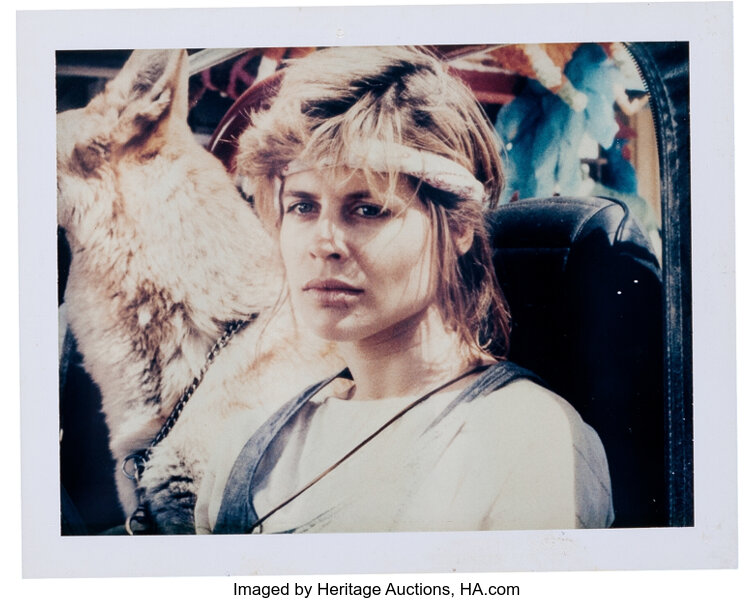 Weathered Polaroid of a figure wrapped in salvaged fur and webbing, staring out from a disrupted timeline.